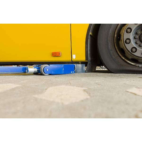 Låg hydraulisk blå domkraft under gul buss på verkstad